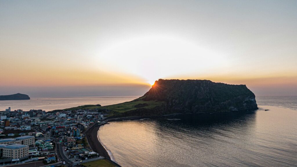 Sunrise beside Seongsan Ilchulbong and the coastal village on Jeju Island.